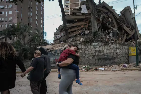 people-walk-past-a-collapsed-building-following-NAEVVMSCRREJVLTZHX6KATGC2U